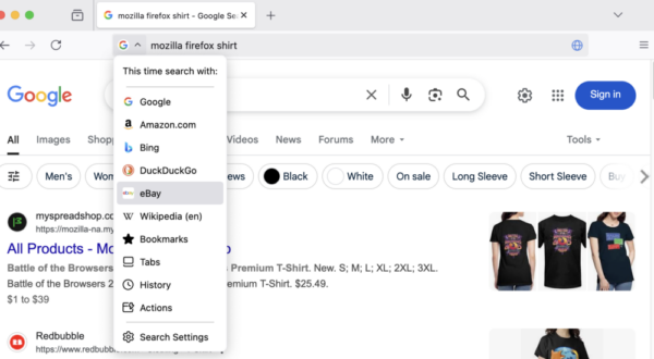 A screenshot of a Google search for “mozilla firefox shirt” in Firefox Nightly, showing the Firefox address bar’s search engine selection feature. The dropdown menu displays alternative search options including Google, Amazon, Bing, DuckDuckGo, eBay, and Wikipedia.